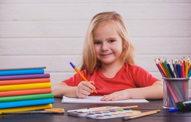 Okula dönüş. Şirin çocuk kapalı masa başında oturuyor. Çocuk beyaz arka plan üzerinde sınıfta öğrenme