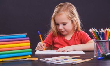 Okula dönelim. Şirin çocuk içeride bir masada oturuyor. Çocuk sınıfta tahtada öğreniyor..