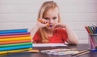 Okula dönüş. Şirin çocuk kapalı masa başında oturuyor. Çocuk beyaz arka plan üzerinde sınıfta öğrenme
