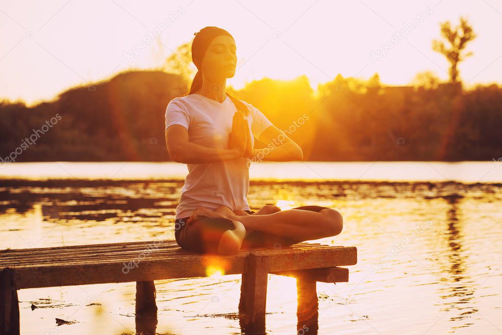 Young brunette woman practicing yoga on the beach at sunset