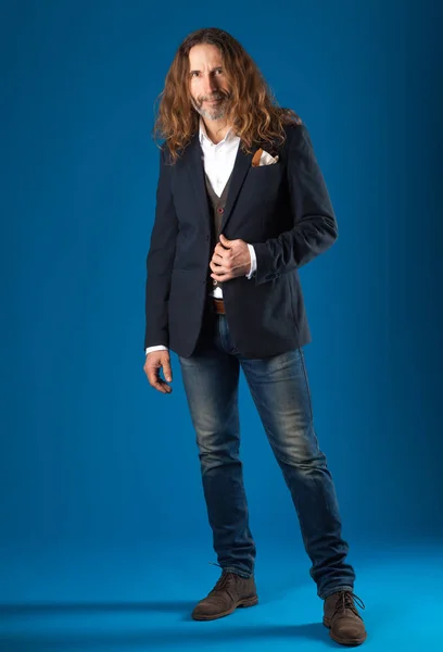 Homem elegante de cabelos longos em jeans e jaqueta em um fundo azul . — Fotografia de Stock