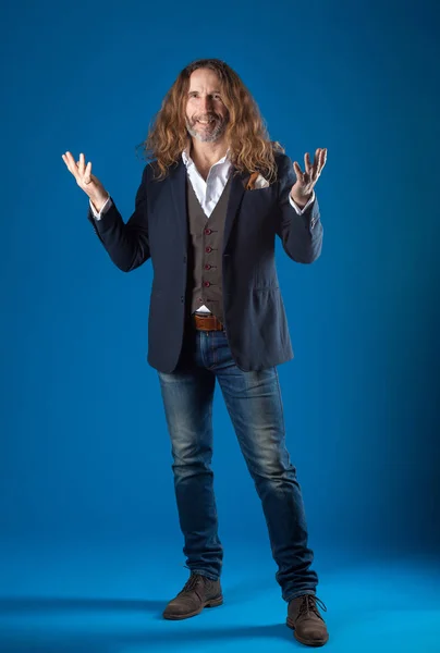 Homem elegante de cabelos longos em jeans e jaqueta em um fundo azul . — Fotografia de Stock