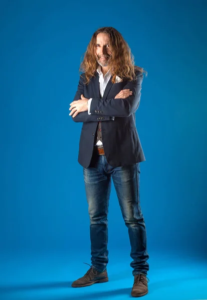 Hombre de pelo largo con estilo en jeans y chaqueta sobre un fondo azul . — Foto de Stock