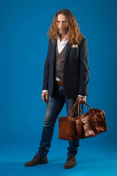Langharige stijlvolle man in spijkerbroek en jasje op een blauwe achtergrond. — Stockfoto