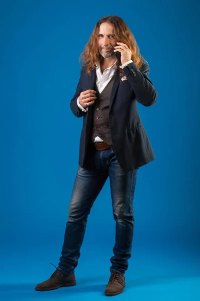 Homem elegante de cabelos longos em jeans e jaqueta em um fundo azul . — Fotografia de Stock