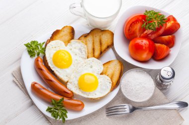 Sevgililer günü - bir kalp ve sosis, süt, Beyaz ahşap masa üzerinde domates şeklinde kızarmış yumurta kahvaltı.