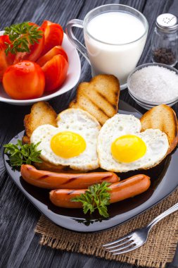 Sevgililer günü - bir kalp ve sosis, süt, siyah ahşap masa üzerinde domates şeklinde kızarmış yumurta kahvaltı.