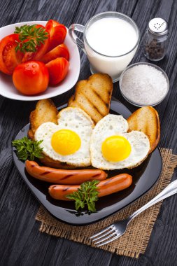 Sevgililer günü - bir kalp ve sosis, süt, siyah ahşap masa üzerinde domates şeklinde kızarmış yumurta kahvaltı.