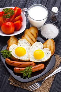 Sevgililer günü - bir kalp ve sosis, süt, siyah ahşap masa üzerinde domates şeklinde kızarmış yumurta kahvaltı.