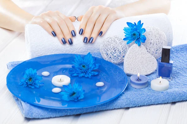 beautiful blue manicure with oil and candles, chrysanthemum and towel on the white wooden table. spa