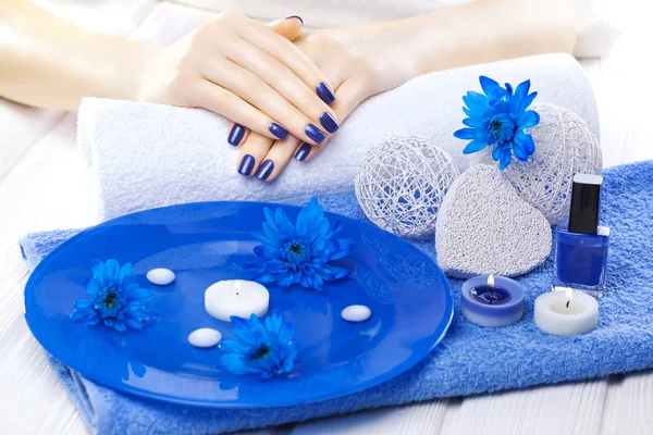 beautiful blue manicure with oil and candles, chrysanthemum and towel on the white wooden table. spa