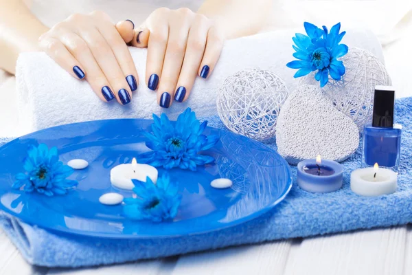 beautiful blue manicure with oil and candles, chrysanthemum and towel on the white wooden table. spa