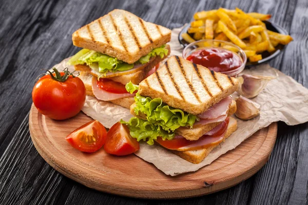 club sandwich with Tomato, lettuce, bacon, ham and french fries on the black wooden table