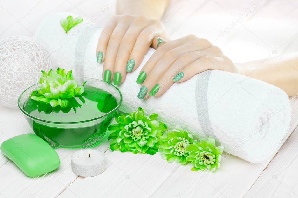 beautiful green manicure with oil and candles, chrysanthemum and towel on the white wooden table. spa