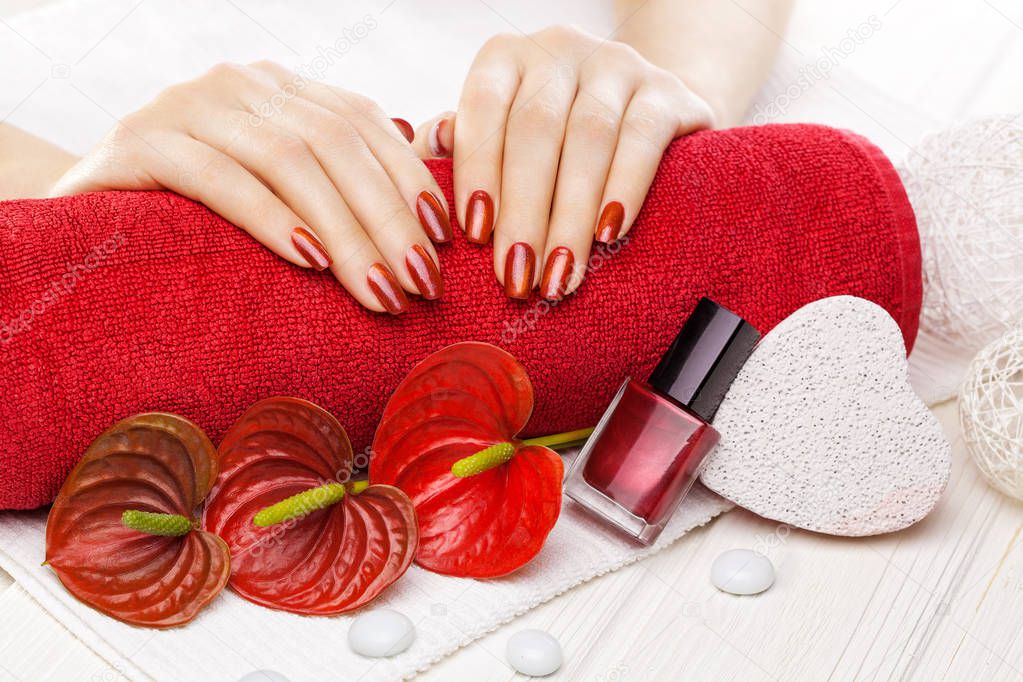 Luxury red manicure with oil and decor, red calla flower and towel on the white wooden table.