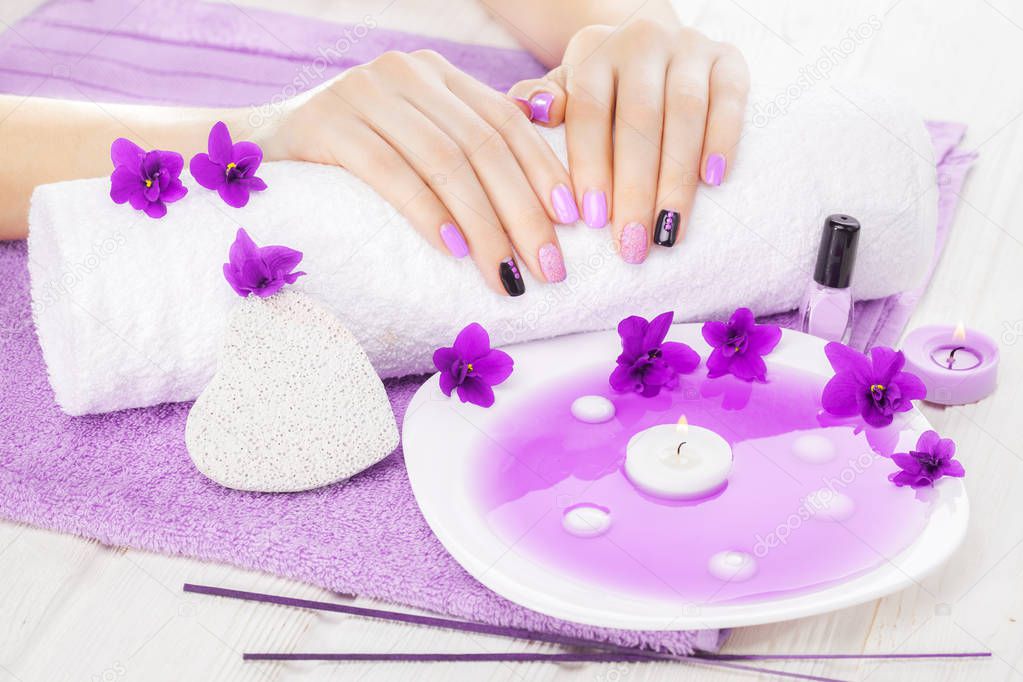beautiful purple manicure with violet, candle and towel on the white wooden table. spa