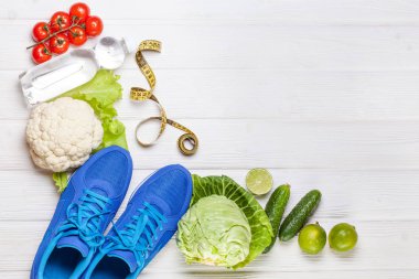 Fitness, aktif yaşam tarzları kavramı. Taze sağlıklı sebze, spor ayakkabı Beyaz ahşap zemin üzerinde. metin için yer kopyalayın. Üstten Görünüm