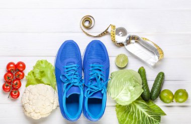 Fitness, aktif yaşam tarzları kavramı. Taze sağlıklı sebze, spor ayakkabı Beyaz ahşap zemin üzerinde. metin için yer kopyalayın. Üstten Görünüm