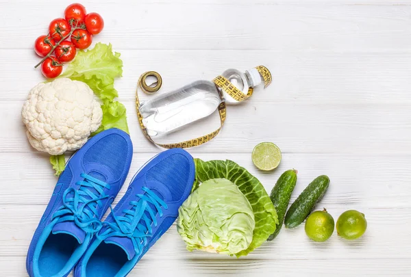 Fitness, active lifestyles Concept. Fresh healthy vegetables, sport shoes on white wood background. copy space for text. Top view