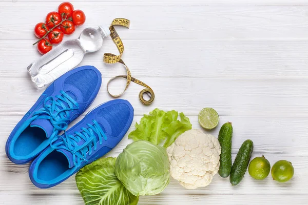 Fitness, active lifestyles Concept. Fresh healthy vegetables, sport shoes on white wood background. copy space for text. Top view