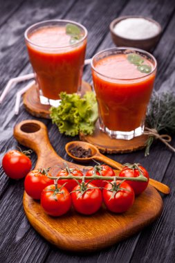 Bardak taze domates suyu ve domates ahşap kesme tahtası üzerinde. Siyah ahşap bir masa üzerinde.