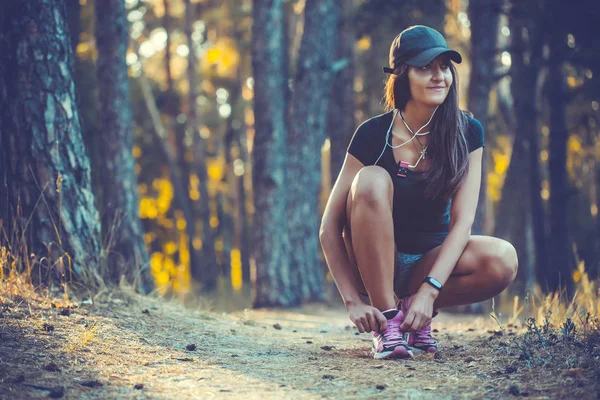 女性ランナー抱き合わせスニーカーの靴ひも 朝の森の中ジョギングします フィットネス — ストック写真