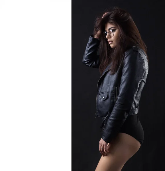 Brunette meisje in een zwarte lederen jas. Mooi model op een donkere achtergrond. — Stockfoto