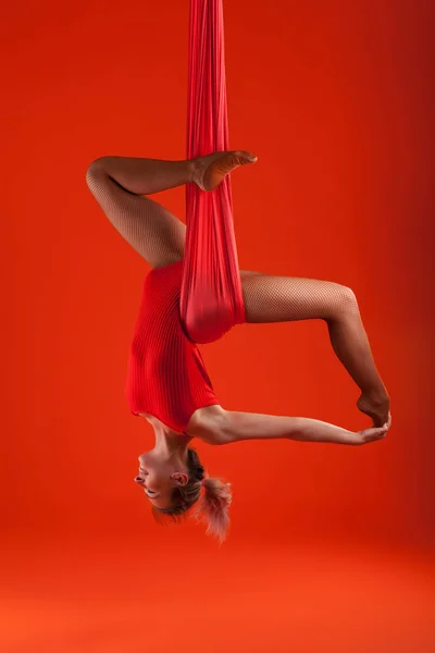 Uma jovem loira com cabelos longos em um terno vermelho realiza ginástica e exercícios em seda . — Fotografia de Stock