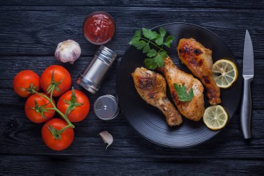 siyah bir tabak üzerinde domates, limon, maydanoz ve ketçap ile tavuk bacakları