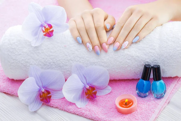 Beautiful colored manicure with orchid, candle and towel on the white wooden table. — Stock Photo, Image