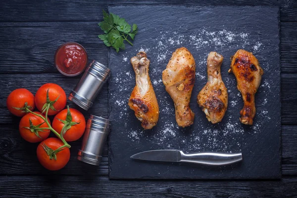 Pernas de frango com tomates, limão, salsa e ketchup em um quadro de ardósia preta — Fotografia de Stock
