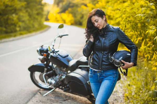 Attractive brunette motorcyclist standing near a motorcycle. — Stock Photo, Image