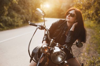 gün batımında bir motosiklet yanında duran çekici esmer motosikletçi.