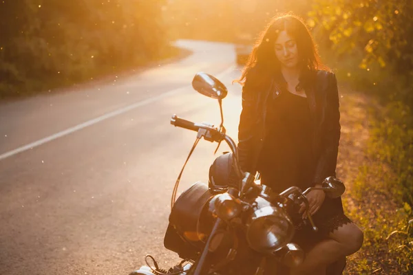 Attrayant brunette motocycliste debout près d'une moto sur le coucher du soleil . — Photo