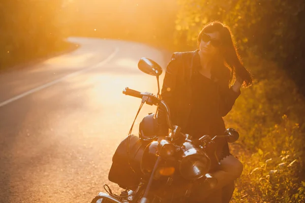 Attrayant brunette motocycliste debout près d'une moto sur le coucher du soleil . — Photo