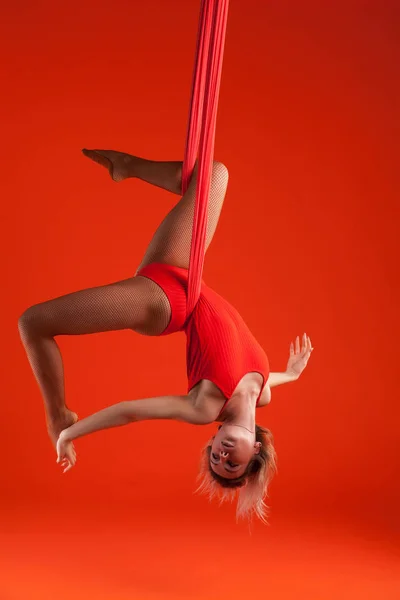 Une jeune fille blonde aux cheveux longs en costume rouge fait du gymnastique et des exercices sur soie . — Photo
