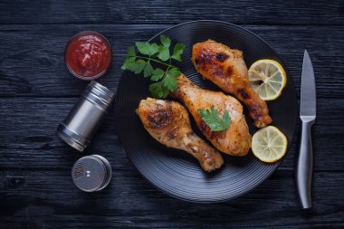 siyah bir tabak üzerinde domates, limon, maydanoz ve ketçap ile tavuk bacakları