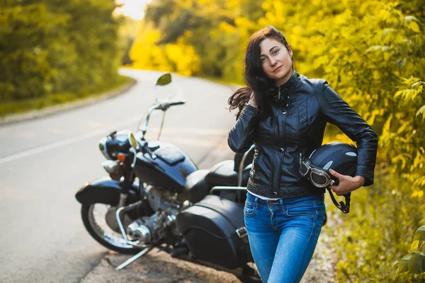 Attractive brunette motorcyclist standing near a motorcycle. — Stock Photo, Image