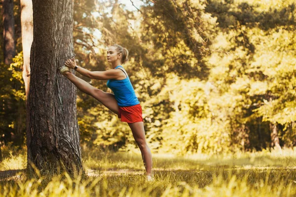 Pretty kvinna atlet gör övningar innan jogging genom skogen — Stockfoto
