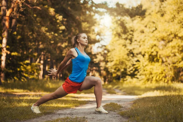 Pretty woman athlete doing exercises before jogging through the woods — Stock Photo, Image