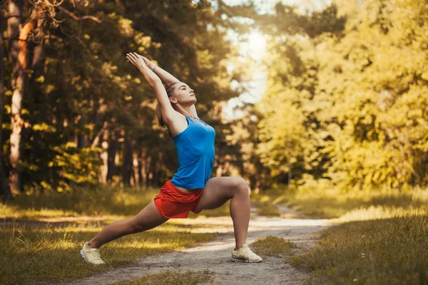 Pretty woman athlete doing exercises before jogging through the woods — Stock Photo, Image