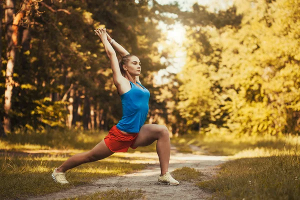 Pretty woman athlete doing exercises before jogging through the woods — Stock Photo, Image