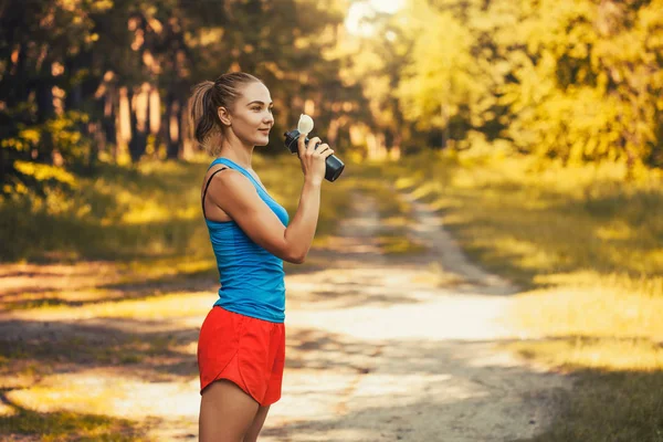 Woman athlete takes a break, she drinking — Stock Photo, Image