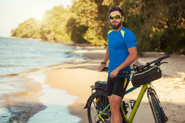 Brodaty człowiek rowerzysta jeździ wzdłuż piaszczystej plaży na rowerze górskim. — Zdjęcie stockowe