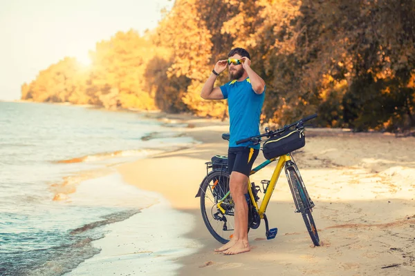 Hombre barbudo ciclista paseos a lo largo de la playa de arena en una bicicleta de montaña . — Foto de Stock