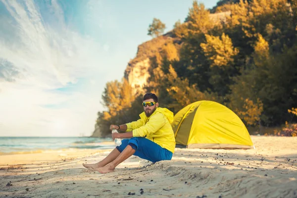 Bebaarde man rusten met een tent op een zandstrand. — Stockfoto