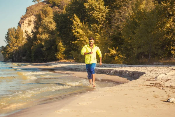 Brodaty sportowiec biegnie wzdłuż piaszczystej plaży. — Zdjęcie stockowe