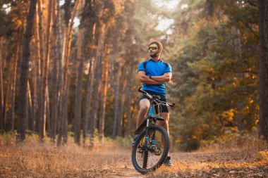 Sakallı adam dağ bisikletiyle ormanda bisiklet sürüyor..