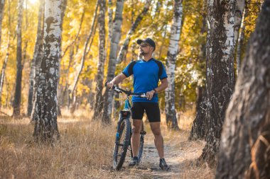 Sakallı adam dağ bisikletiyle ormanda bisiklet sürüyor..