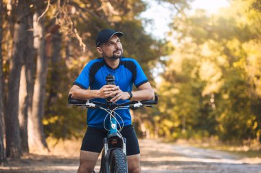 Sakallı adam dağ bisikletiyle ormanda bisiklet sürüyor..